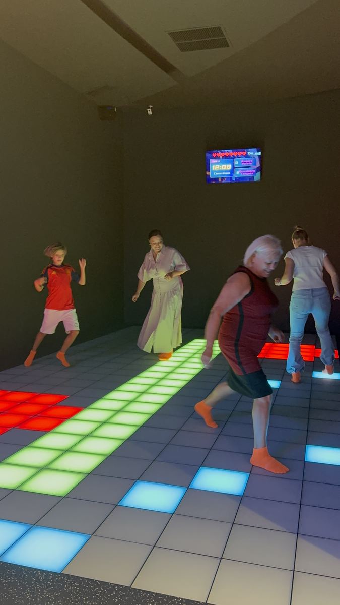Adulți jucând pe podeaua LED interactivă la Hai Pixel din Chișinău, un jucător pășind pe un rând de plăci verzi aprinse