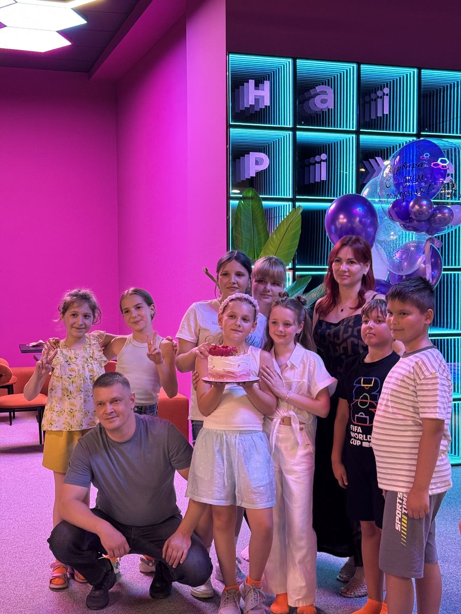 Grup mare de copii și părinți cu baloane în fața peretelui cu litere neon Hai Pixel din Chișinău