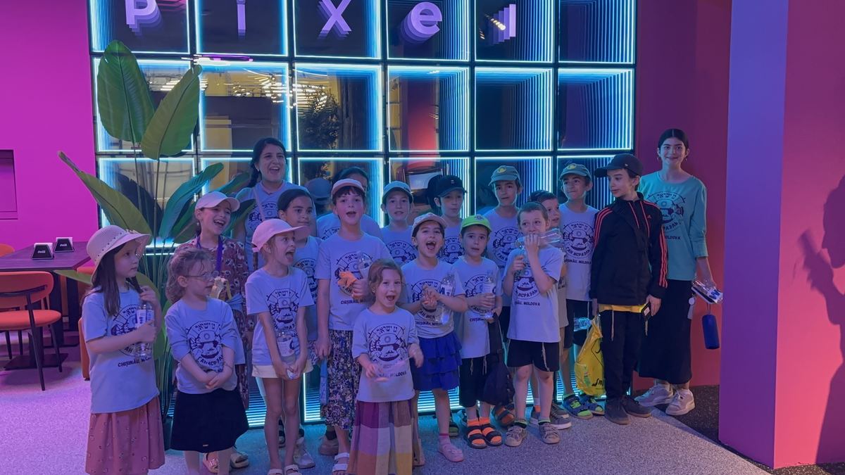 Grup mare de copii în tricouri identice, în fața peretelui cu litere neon Pixel, la Hai Pixel Chișinău