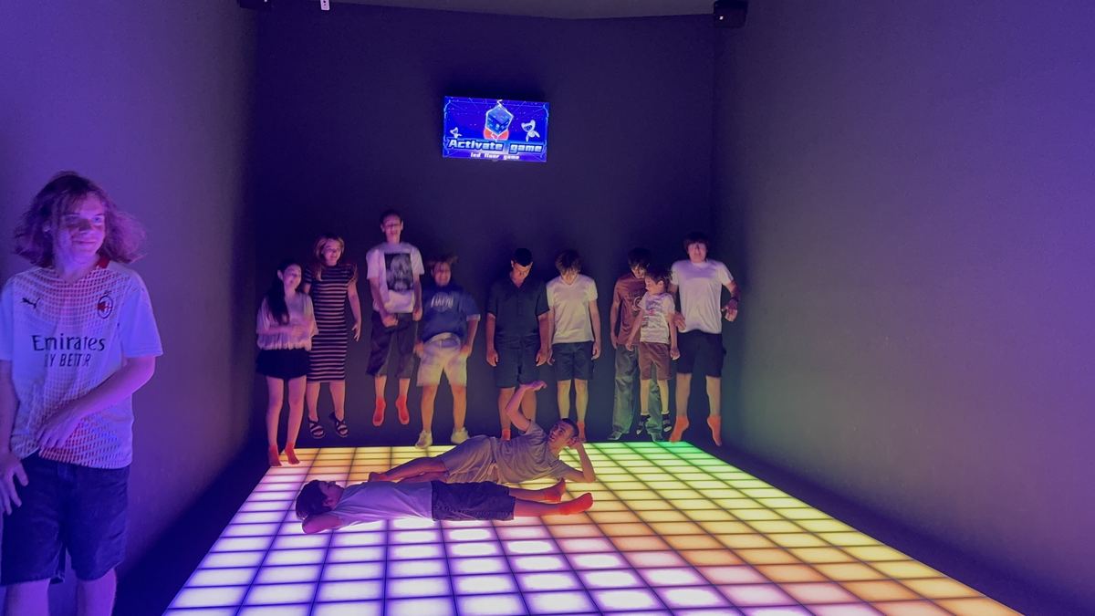 Grup mare de copii jucând pe podeaua LED multicoloră de la Hai Pixel Chișinău, cu monitorul de scor deasupra