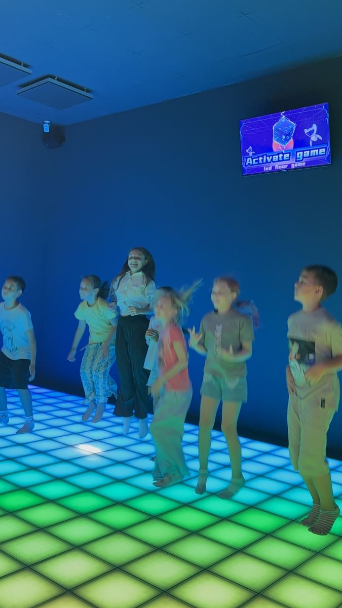 Grup de tineri jucând pe podeaua LED interactivă luminată în degrade verde și galben la Hai Pixel, Chișinău