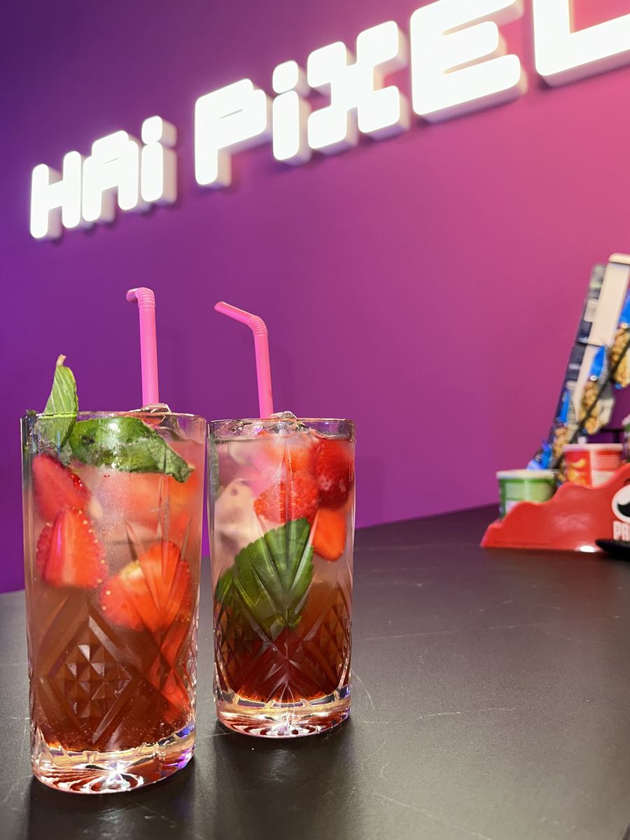 Două pahare de limonadă cu căpșune și mentă pe barul de la Hai Pixel Chișinău, cu firma neon roz Hai Pixel în spate