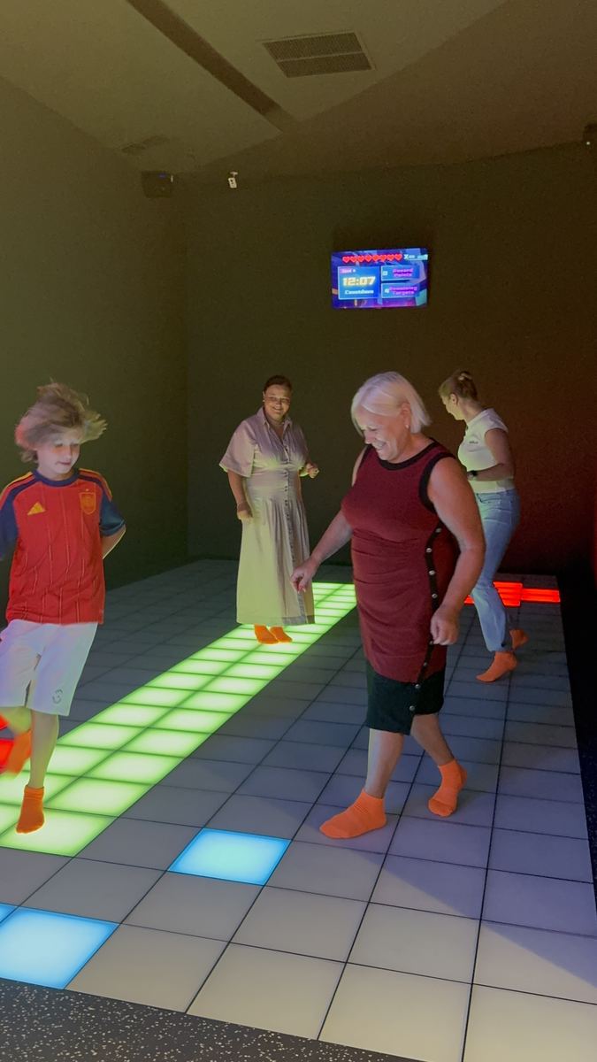 Grup de adulți de vârste diferite jucând împreună pe podeaua LED verde și albă la Hai Pixel, Chișinău