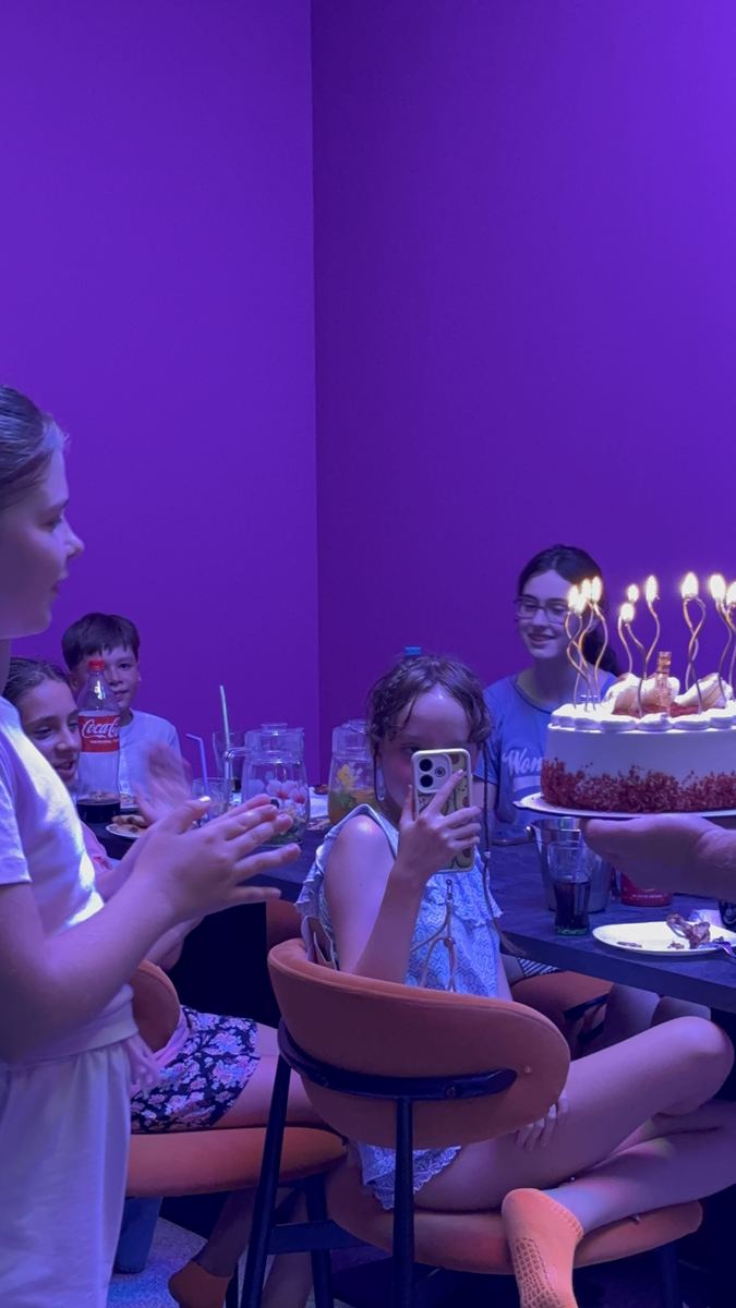 Tort aniversar cu lumânări aprinse pe masa din zona de celebrare de la Hai Pixel Chișinău, sub lumini violet